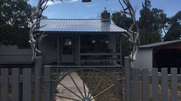 A metal gate with a large wheel, a deer head sculpture, and a house in the background.