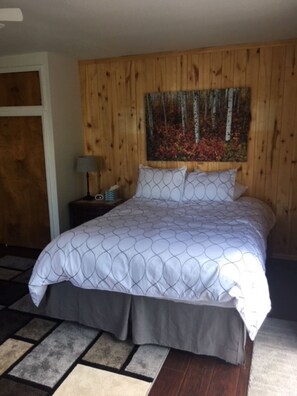 A bedroom with a wooden headboard, a bed with a patterned bedspread, a nightstand with a lamp, and a painting of a forest scene. - The Golden Getaway, #A (Crestone)