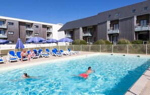 Una piscina con sillas de descanso y sombrillas, rodeada por un edificio con balcones.