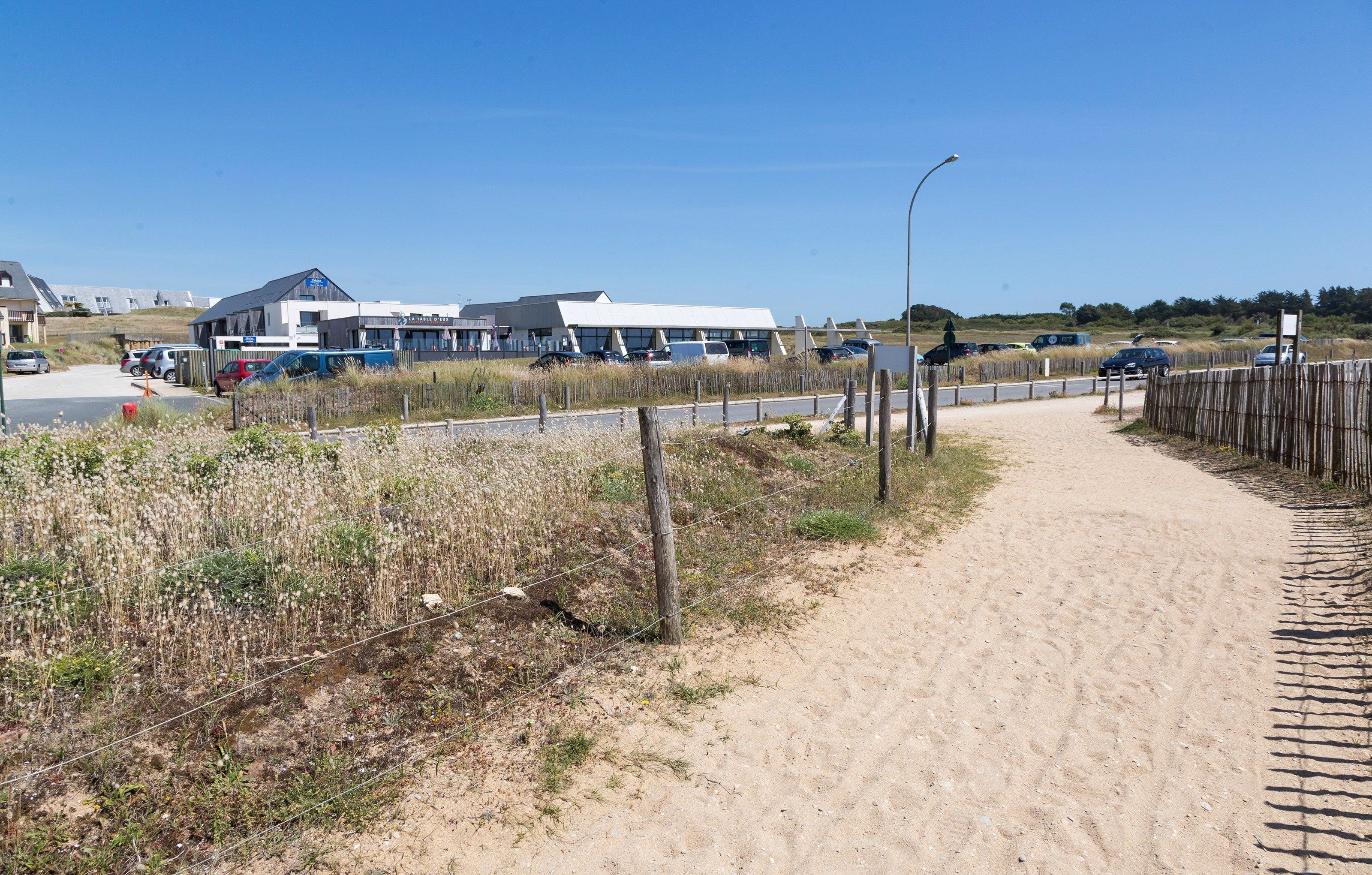 A sandy path leading to a building with a white roof and multiple windows.