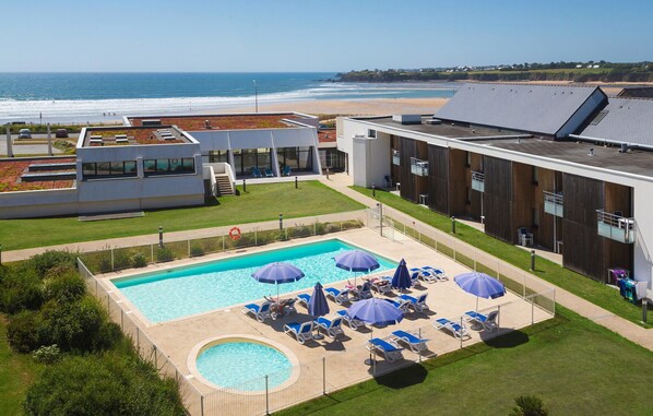 Un hotel moderno con piscina, sillas de descanso y vistas a la playa.