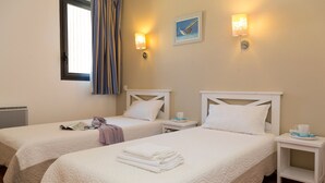 Habitación de hotel con dos camas, una ventana con cortinas, luces fijadas a la pared y una mesita con taza y platillo.