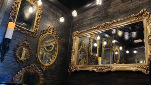 A bathroom with ornate gold-framed mirrors, a bathtub, and a black brick wall. - The Dorm Room (Chickamauga)