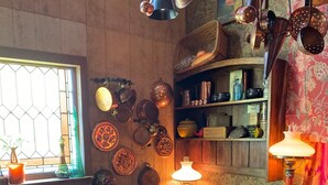 A rustic kitchen with wooden cabinets, a dining table, and various kitchen utensils hanging on the wall. - The Dorm Room (Chickamauga)