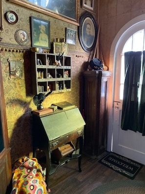 A vintage room with a wooden desk, shelves with various items, and a door with a welcome mat.