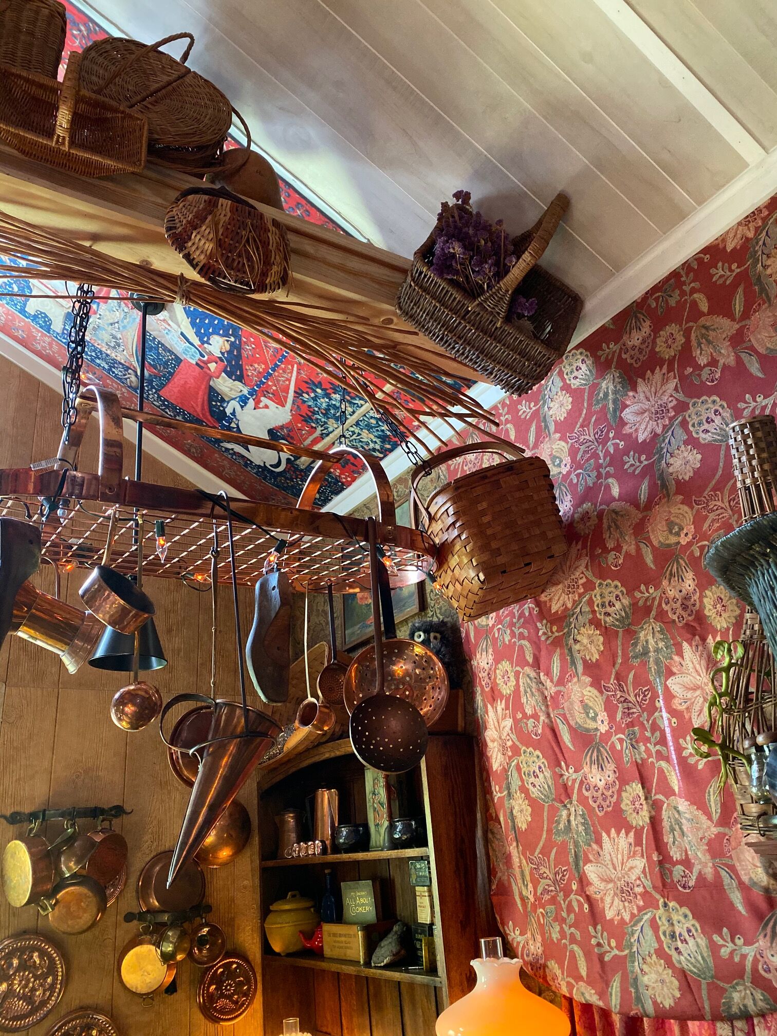 A kitchen with hanging copper cookware, wicker baskets, and a floral-patterned wall.