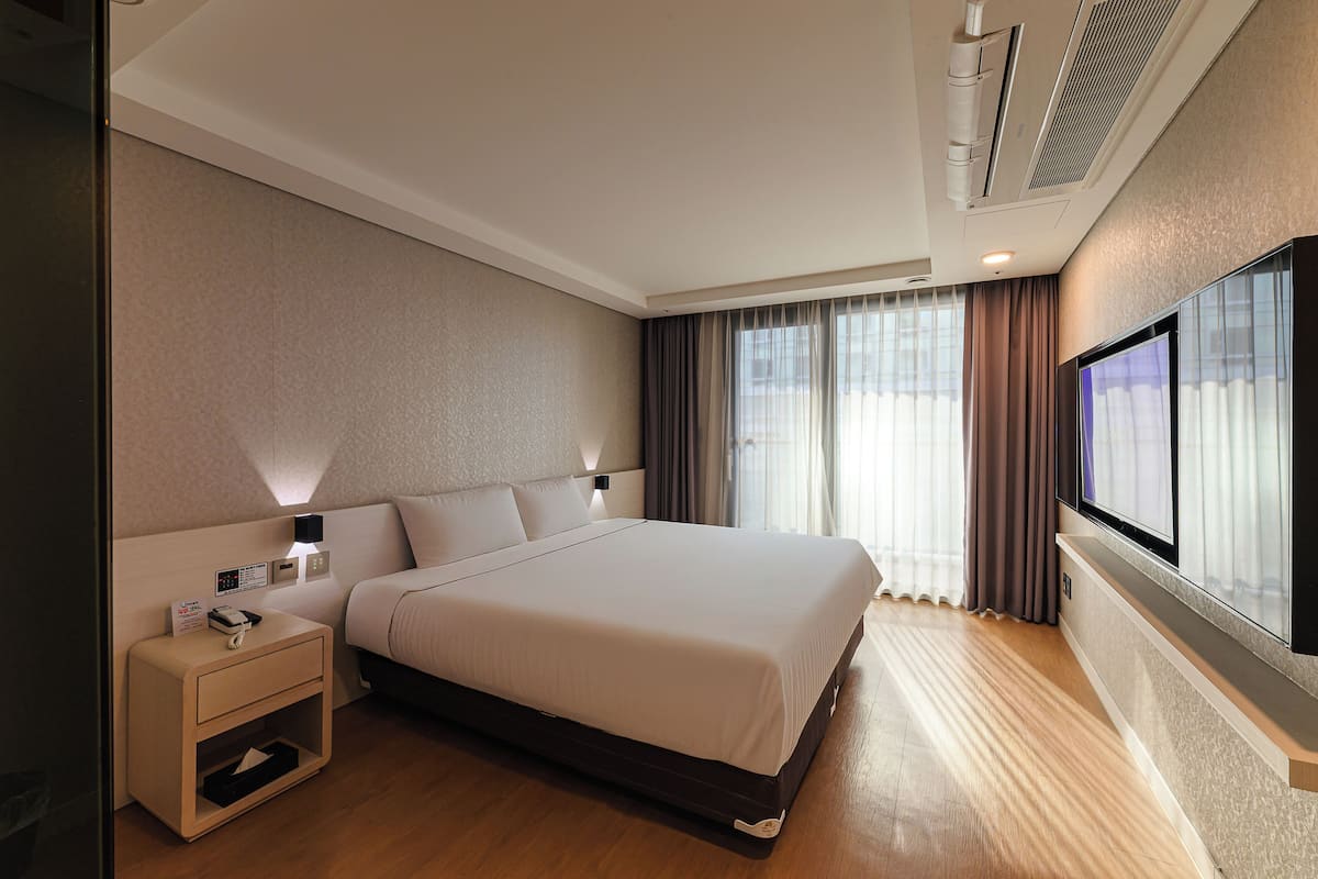 Habitación de hotel con una cama grande, mesitas de noche, televisor y ventana con cortinas.