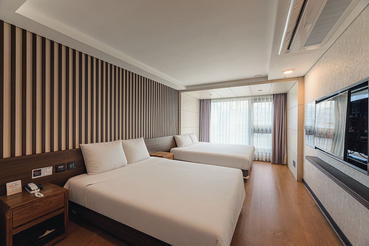 Habitación de hotel con dos camas, cabecera de madera, televisor de pantalla plana y ventana con cortinas.
