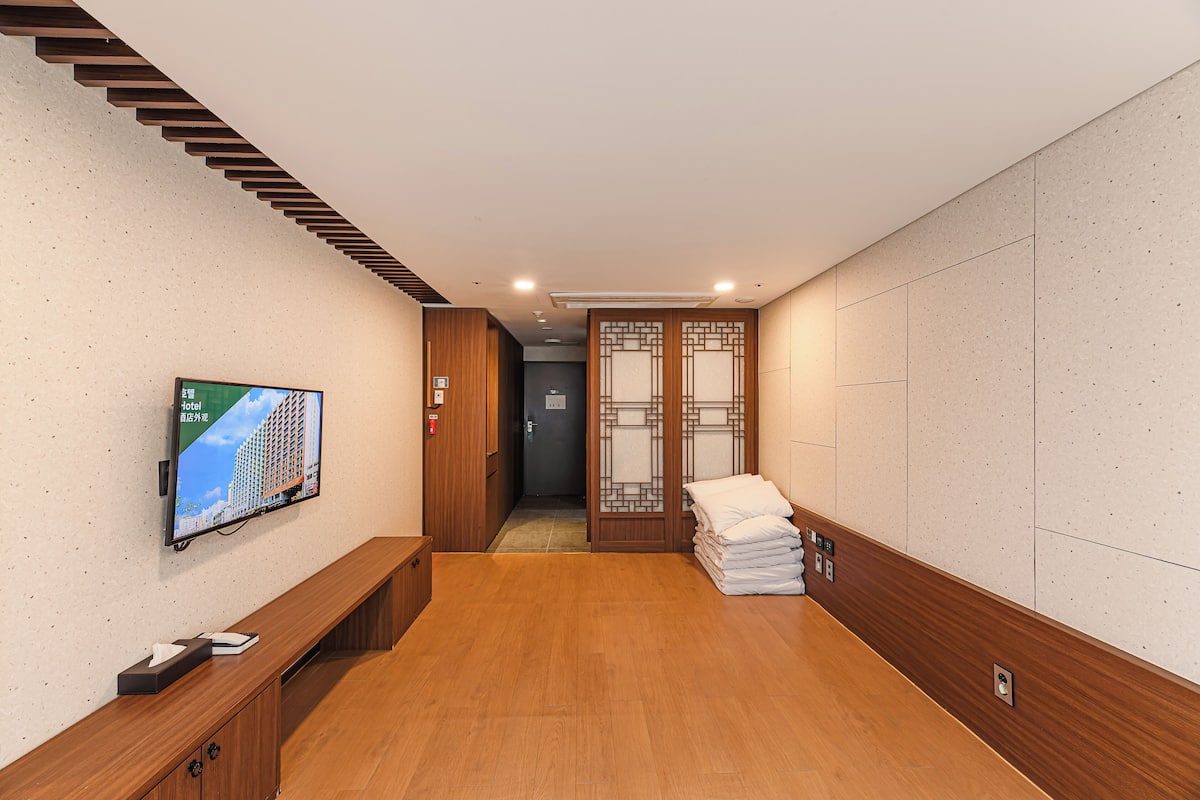 Un pasillo de hotel con piso de madera, un televisor montado en la pared, un banco de madera y una pila de toallas blancas.