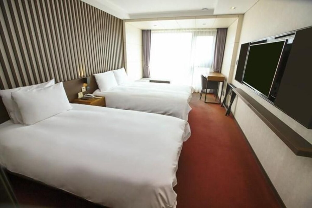 Een hotelkamer met twee bedden, een televisie en een raam met gordijnen.