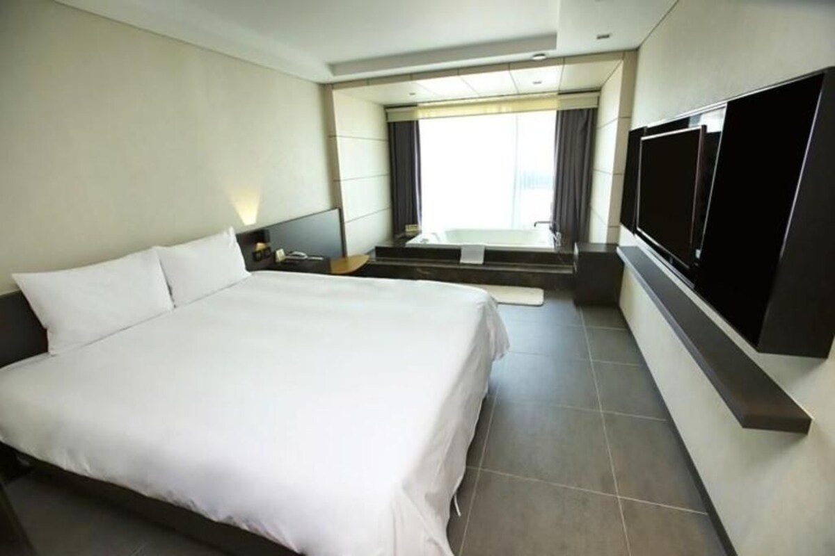 Ein modernes Hotelzimmer mit einem großen Bett, einem an der Wand befestigten Flachbildfernseher und Blick auf die Stadt.