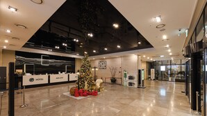 Un hall d’entrée spacieux, décoré d’un sapin de Noël, avec des comptoirs d’accueil et un design moderne au niveau du plafond.