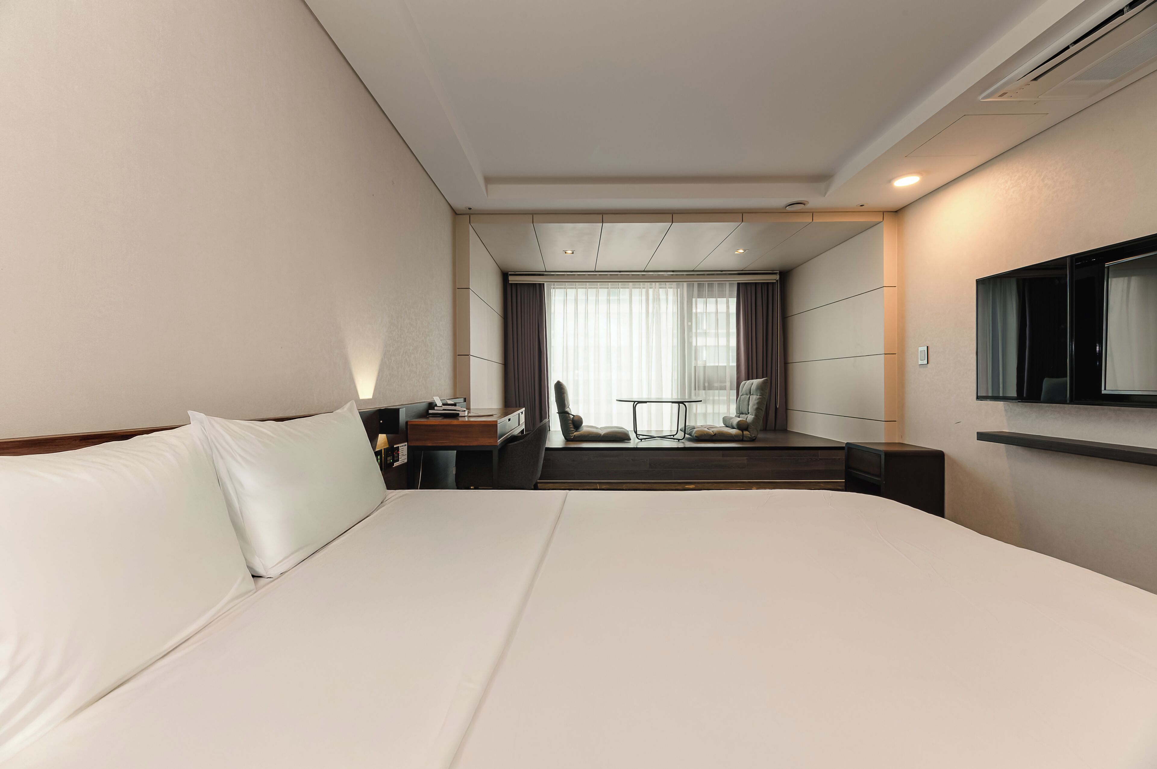 Quarto de hotel moderno com uma cama grande, uma escrivaninha, uma cadeira e uma televisão.