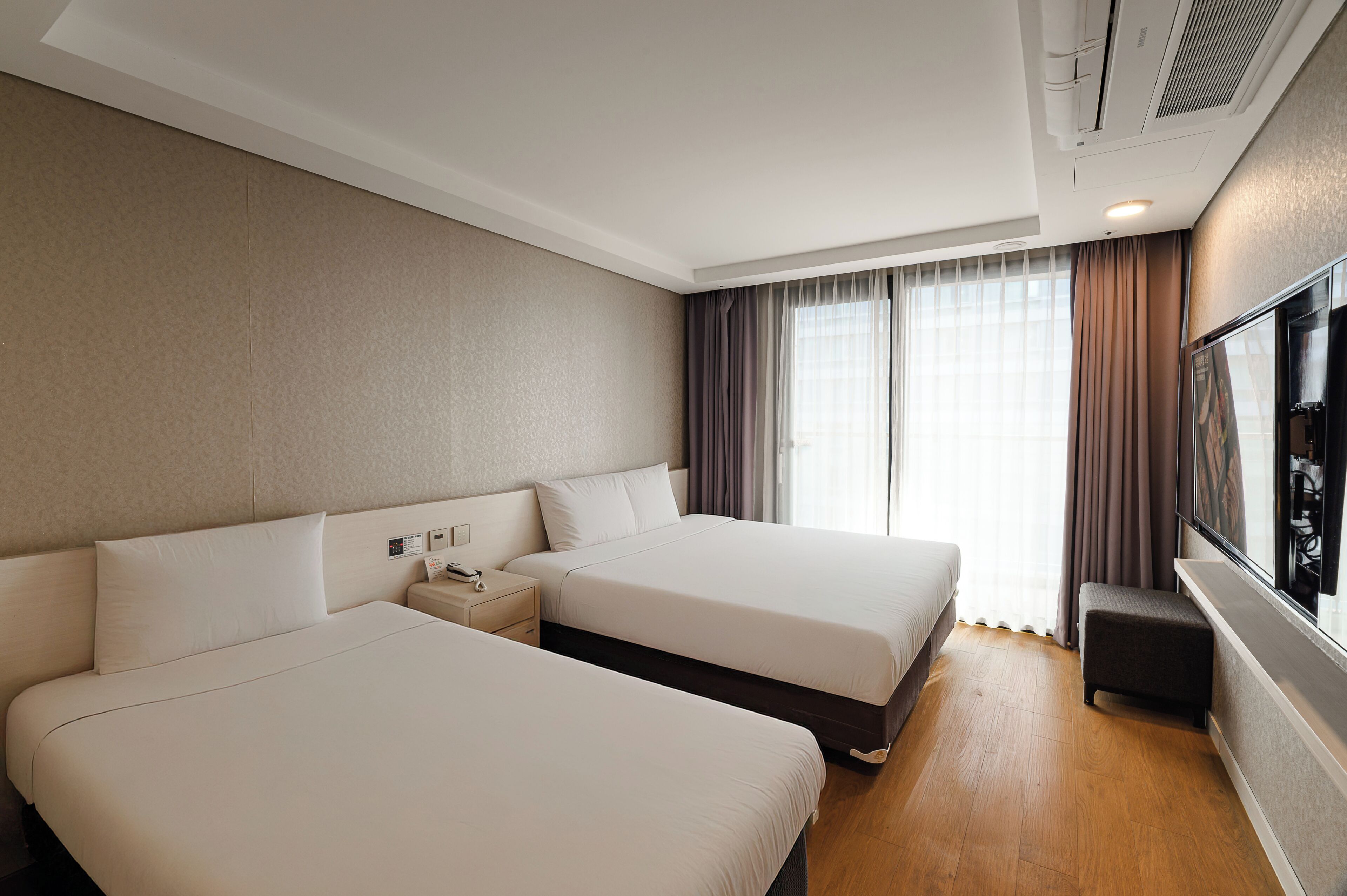 A hotel room with two beds, a nightstand, a TV, and a window with curtains.