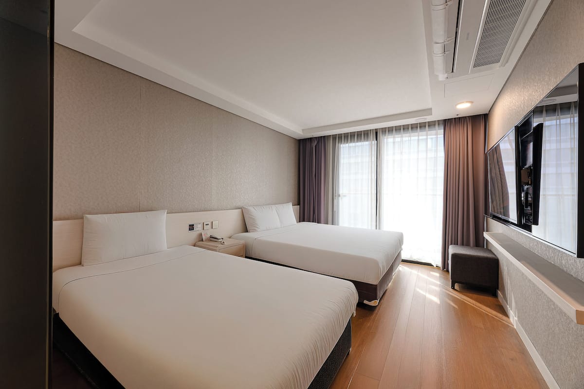Habitación de hotel con dos camas, televisión y un amplio ventanal con cortinas.