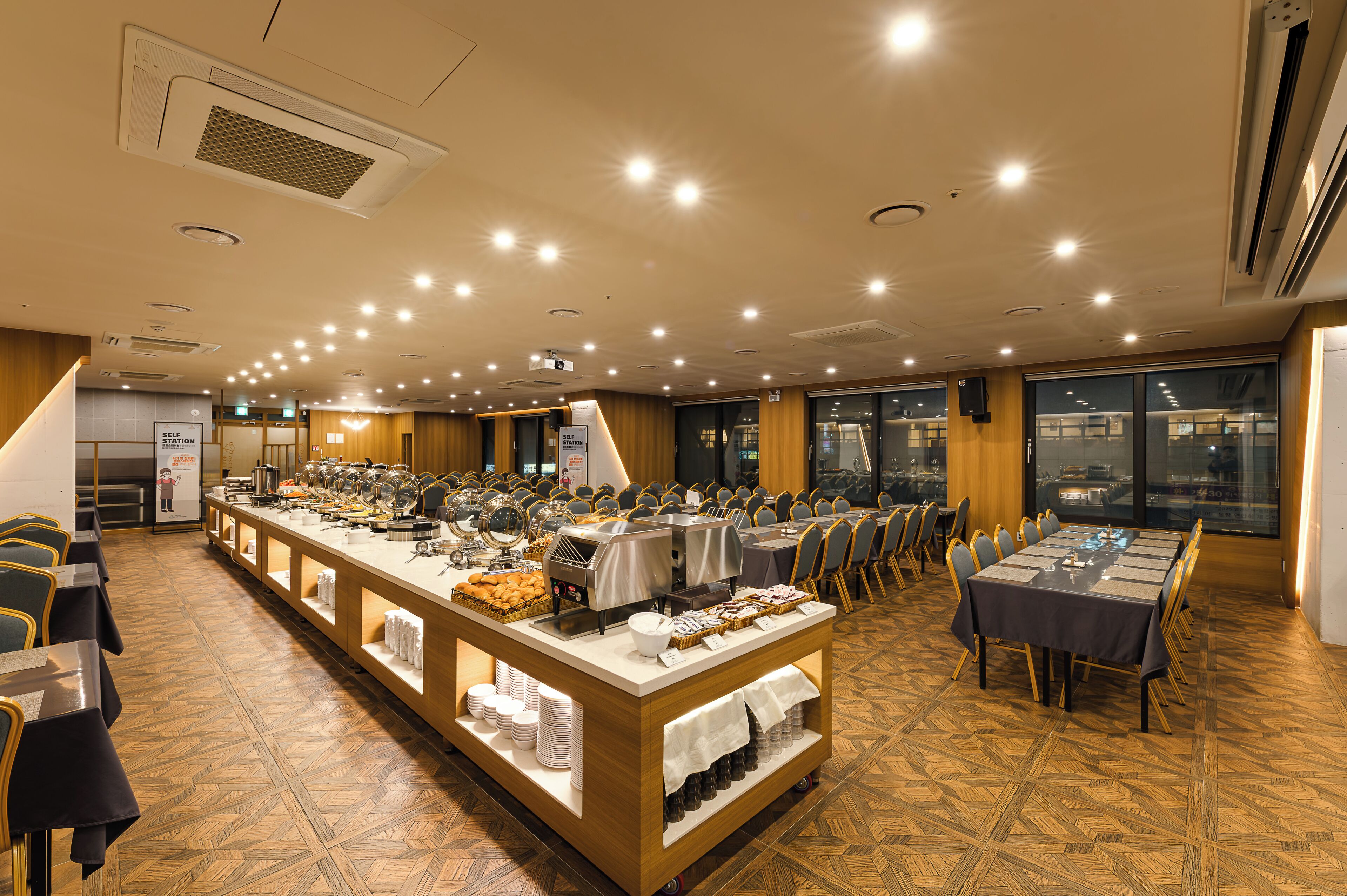A buffet setup with multiple food stations, a self-service station, and a dining area with tables and chairs.