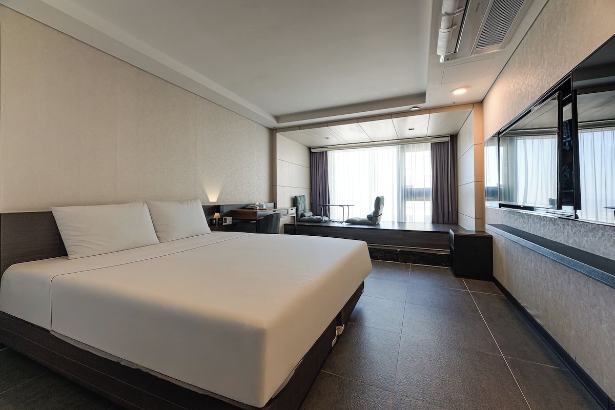 Una habitación de hotel moderna con una cama grande, un escritorio y vistas a la ciudad a través de amplios ventanales.