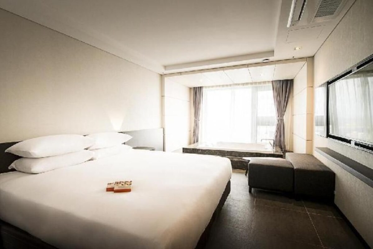 Een moderne hotelkamer met een groot bed, een zithoekje, een raam met gordijnen en uitzicht op de omgeving.