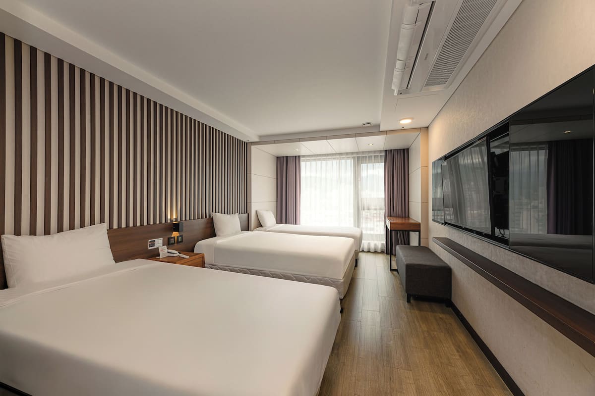 Habitación de hotel con dos camas, televisión, escritorio y un ventanal con cortinas.