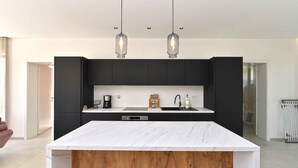 Une cuisine moderne dot ée d’un plan de travail en marbre, de meubles noirs et de deux luminaires suspendus.