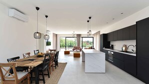 Une cuisine moderne dotée d’un îlot central, de meubles de rangement aux couleurs sombres et d’un éclairage suspendu.