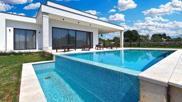 Une maison moderne dotée d’une piscine, de grandes fenêtres et d’une pelouse bien entretenue.