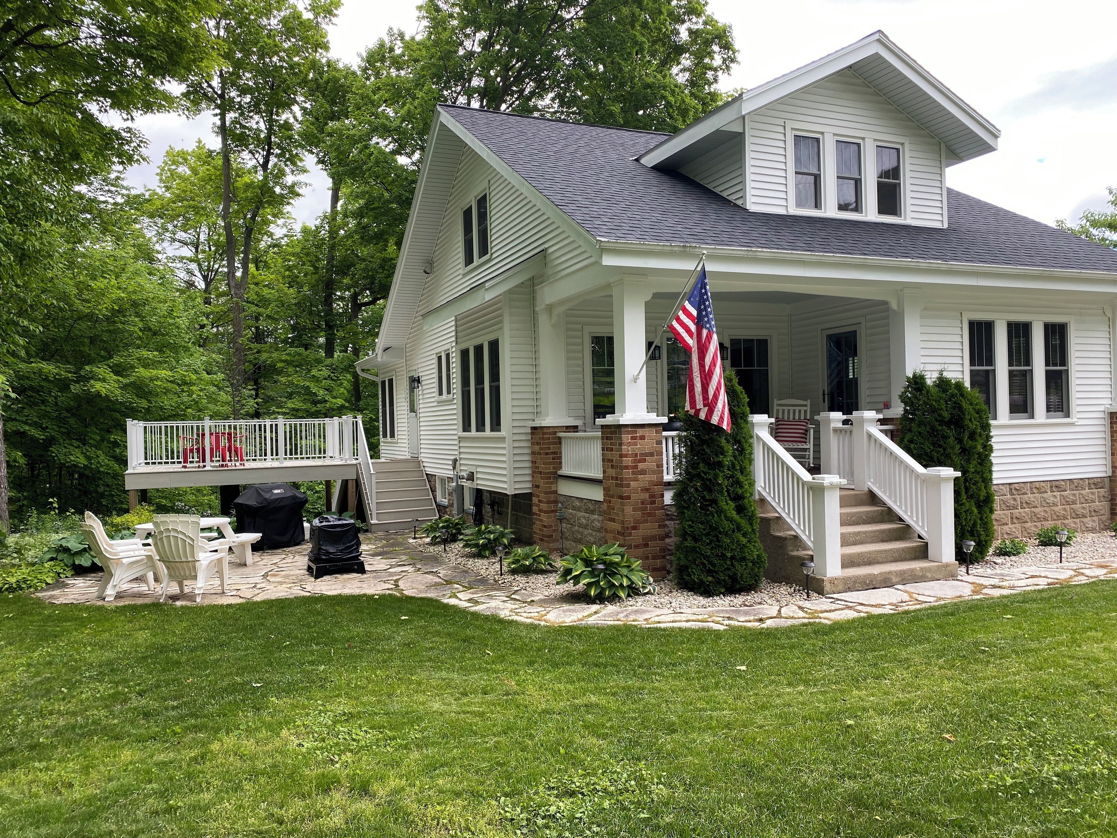 Une maison à deux étages avec un porche, un drapeau et une terrasse avec des chaises.