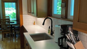 Una cocina con armarios de madera, encimera blanca, un lavamanos, una cafetera y un bloque de cuchillos.