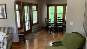 Un salón amplio con un sillón verde, un sofá a rayas y una mesa de comedor con sillas.