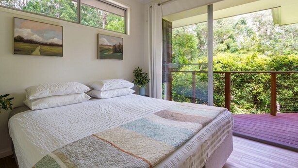 Ein Schlafzimmer mit einem großen Bett, zwei Gemälden, einem Fenster und einem Balkon mit Blick auf Grünflächen.