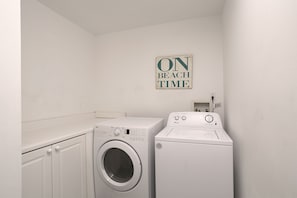A laundry room with two white washing machines, a wall-mounted sign that reads "ON BEACH TIME", and a power outlet on the wall. - Amalfi Coast 311A - Gulf View, Heated Community Pool, Exercise Room, Tennis! (Miramar Beach)