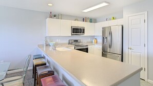 Una cucina moderna con mobili bianchi, elettrodomestici in acciaio inossidabile e un'isola centrale con sgabelli da bar.