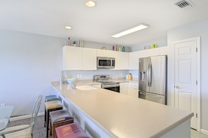 A modern kitchen with white cabinets, stainless steel appliances, and a central island with bar stools. - Amalfi Coast 311A - Gulf View, Heated Community Pool, Exercise Room, Tennis! (Miramar Beach)