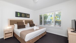 Ein Hotelzimmer mit Bett, Nachttischen, einem Fernseher und einem Fenster mit Jalousien.