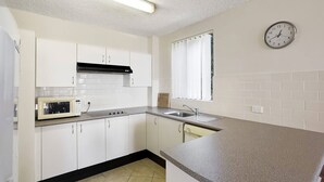 Una cocina compacta con armarios blancos, un microondas, una estufa y un lavamanos.