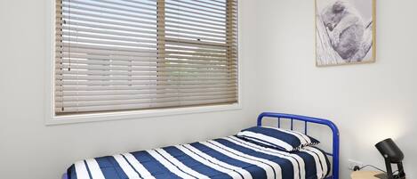 A single bed with a blue metal frame, a striped bedspread, and a bedside lamp on a wooden nightstand.