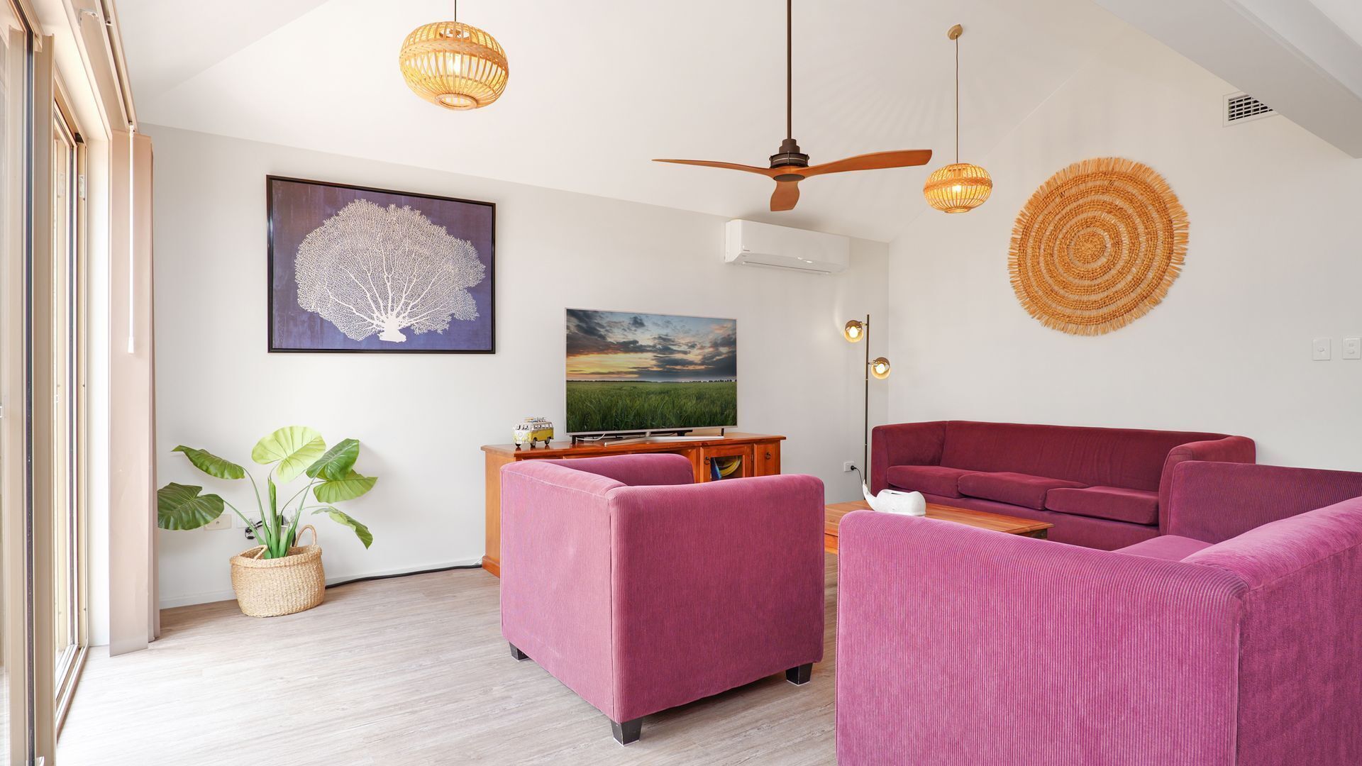 A modern living room with a ceiling fan, a flat-screen TV, and a large painting.