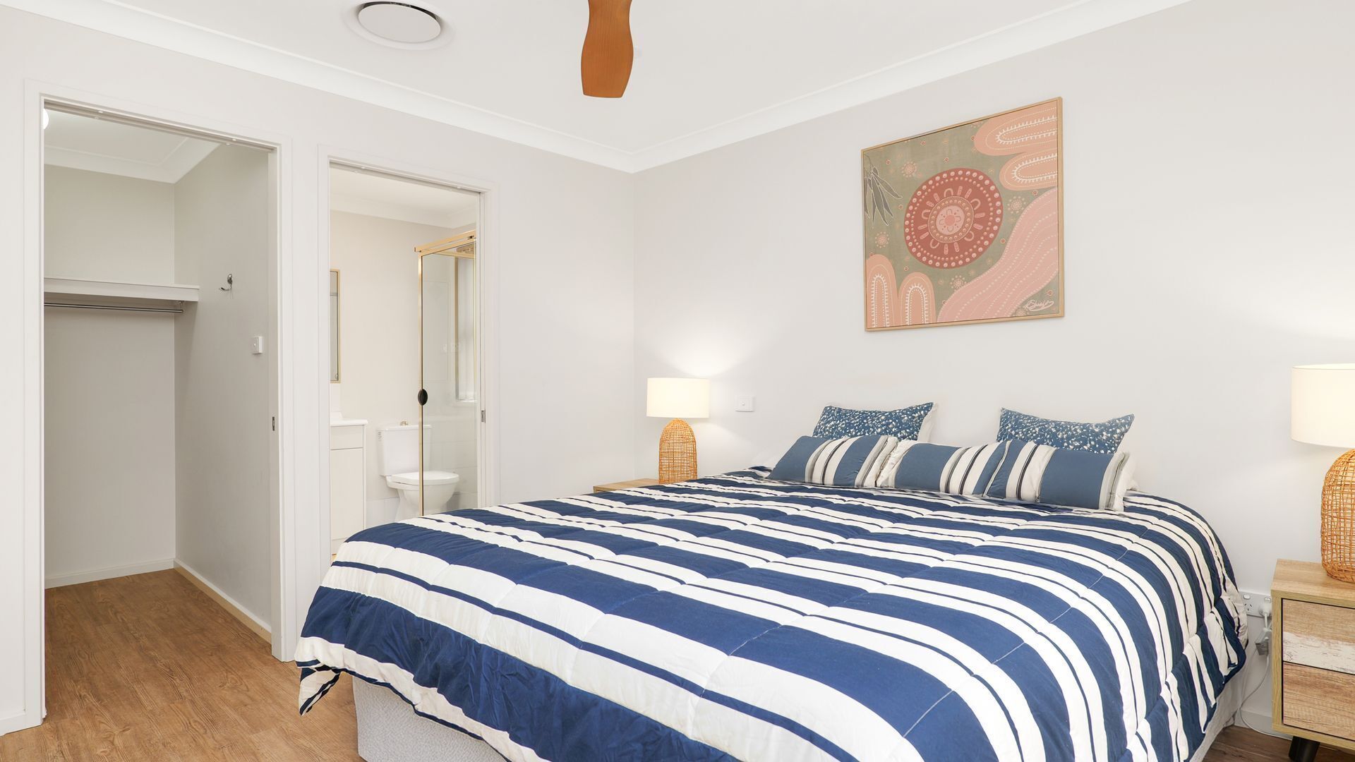 A bedroom with a bed, bedside tables, a wall-mounted lamp, and a door leading to a bathroom.