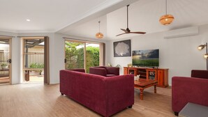 Een ruime woonkamer met een grote televisie, rode banken en een houten salontafel.