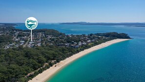 Vue aérienne d’une ville côtière avec une plage, des zones résidentielles et un logo représentant une baleine et des vagues.