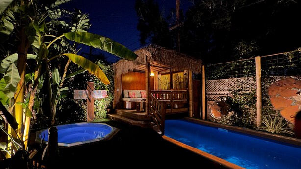 Un espace piscine comprenant un jacuzzi, une terrasse en bois et une structure à toit de chaume.