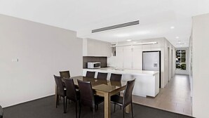 A modern kitchen with white cabinets, a central island, and a dining area with a wooden table and chairs. - Cote D Azur in the heart on Nelson Bay with a swimming pool (Nelson Bay)