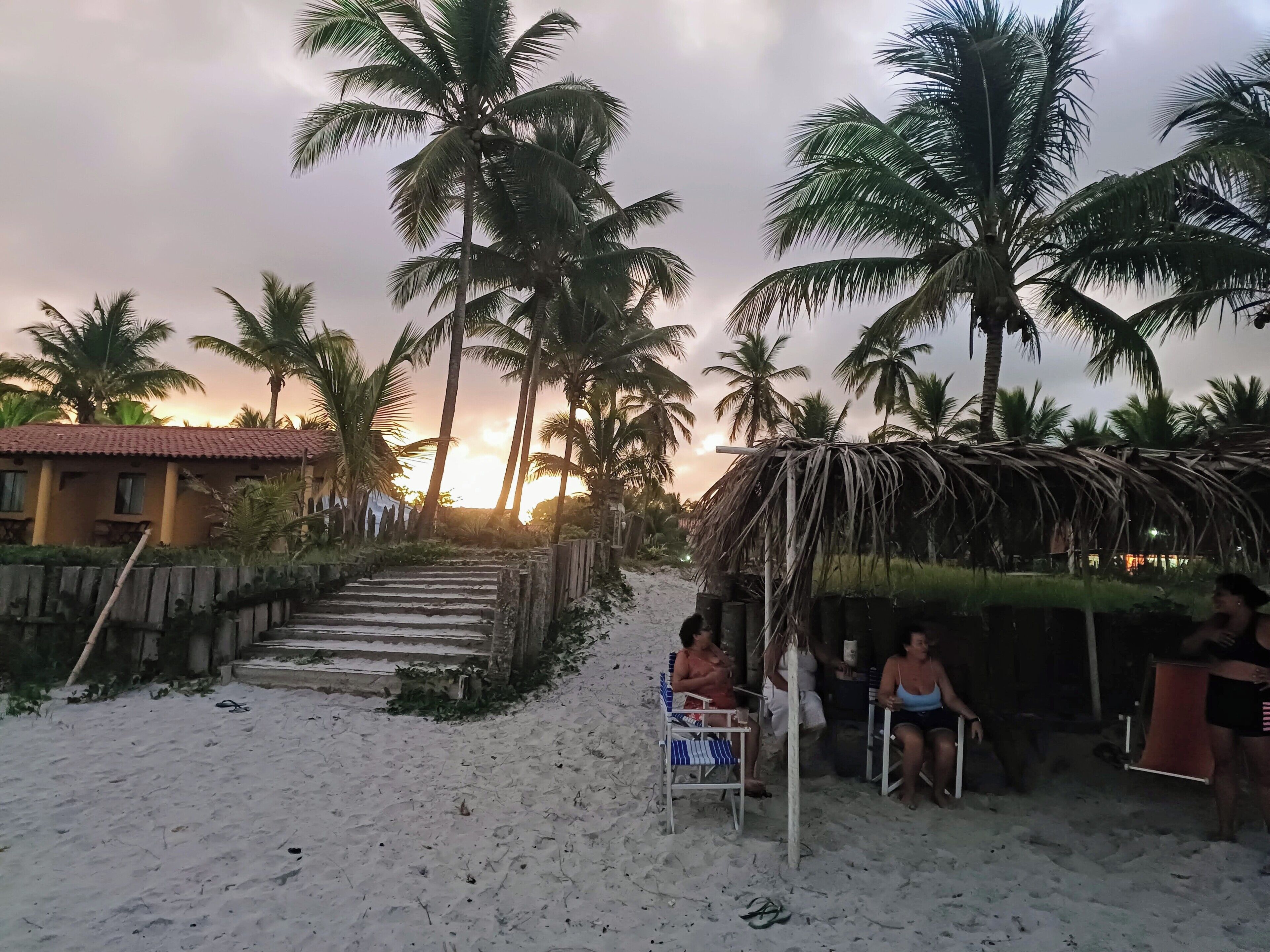 A beach scene with palm trees, a thatched hut, and a building with a red roof.