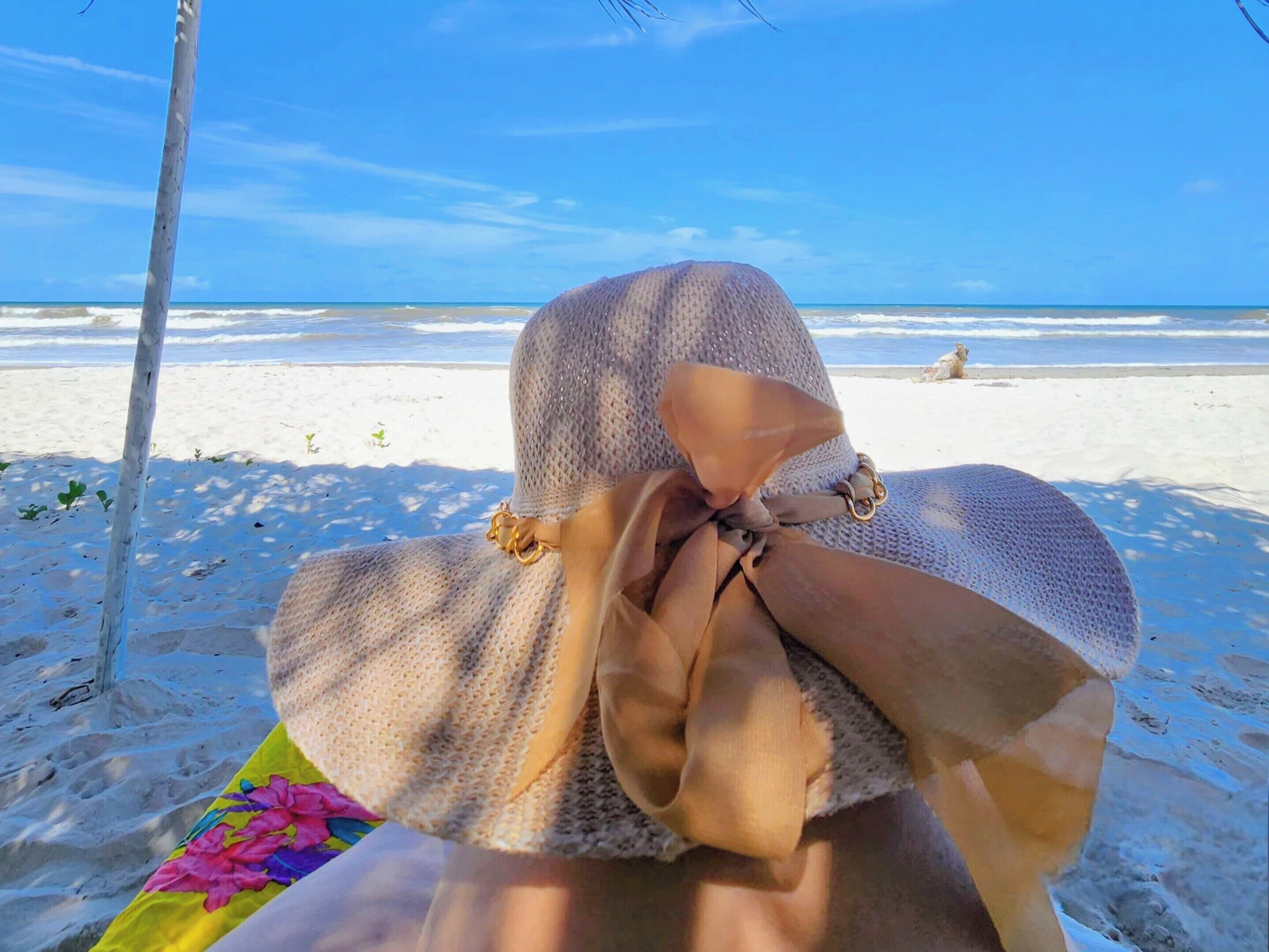A beach scene with a person lying on a blanket, a beach chair, and a clear view of the ocean.