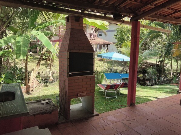 Estrutura de forno construída em tijolos, com vista para um jardim e uma casa ao fundo.