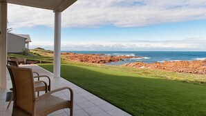 Eine überdachte Terrasse mit Korbstühlen, Blick auf den Ozean und eine felsige Küstenlinie.