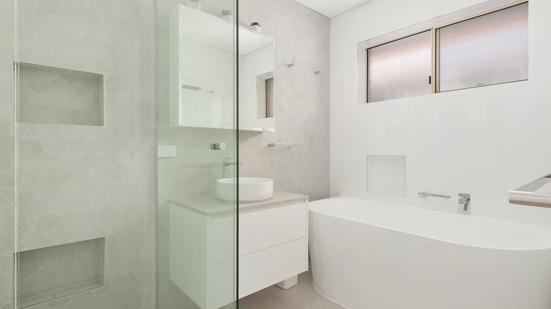 Un baño moderno con cabina de ducha de vidrio, una bañera independiente y un lavamanos con espejo.