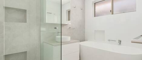 Un baño moderno con cabina de ducha de vidrio, una bañera independiente y un lavamanos con espejo.
