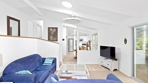 A modern living room with a blue sofa, a glass coffee table, and a flat-screen TV. - Hidden Oasis Pet Friendly In Anna Bay (Anna Bay)