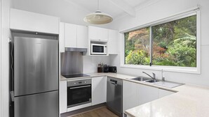 A modern kitchen with stainless steel appliances, a microwave, and a window with a view of greenery. - Hidden Oasis Pet Friendly In Anna Bay (Anna Bay)